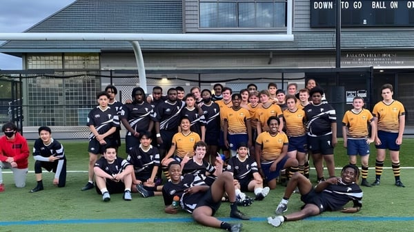 Un grupo de estudiantes de la Cambridge Rindge and Latin High School posan como equipo deportivo en un césped frente a un edificio.