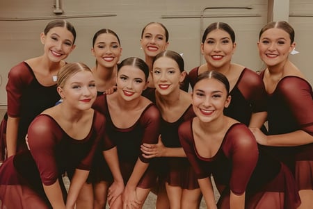 Un grupo de alumnas de la Campo Verde High School posan en un escenario con vestidos rojos y negros.