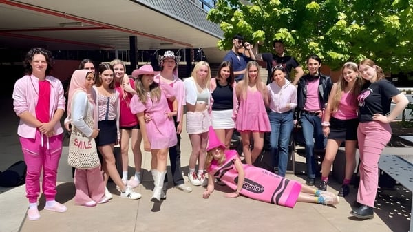 Un grupo de jóvenes mujeres en diferentes tonos de rosa está de pie frente a un edificio en el campus del Canberra College.