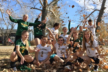 Un grupo de estudiantes de la Canmore Collegiate High School se reúne en un parque con hojas otoñales bajo un cielo azul.