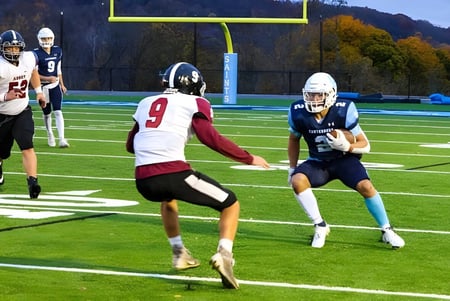Dos jugadores de fútbol americano corren en el campo de Canterbury School con hojas de otoño de fondo.