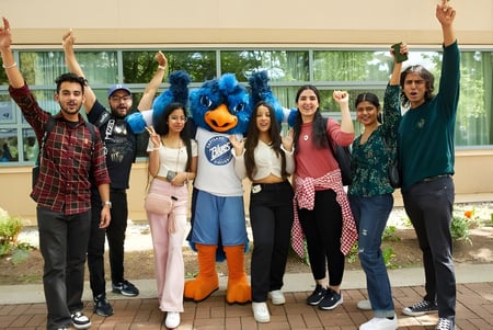 Un grupo de jóvenes se encuentra con los brazos en alto frente a un edificio en el campus de la Capilano University.