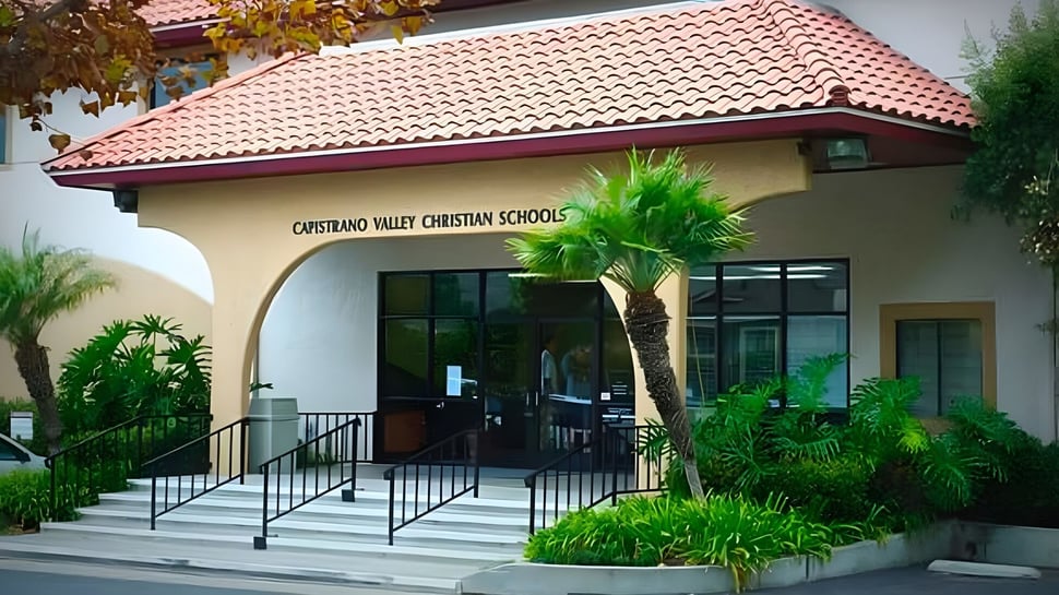 La entrada del edificio de la Capistrano Valley Christian School con techo de tejas rojas y palmeras en primer plano.