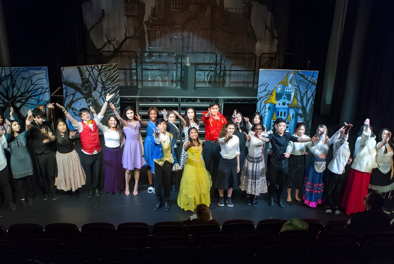 Un grupo de estudiantes del Cardiff Sixth Form College actúa con trajes coloridos en un escenario frente a un fondo de bosque.