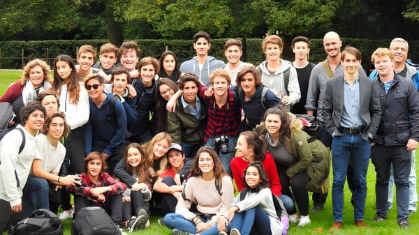 Un grupo de estudiantes del Carfax College se reúne al aire libre frente a árboles y áreas verdes.