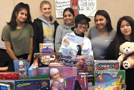Un grupo de alumnas sonrientes está con juguetes y regalos en un aula de la Cariboo Hill School.