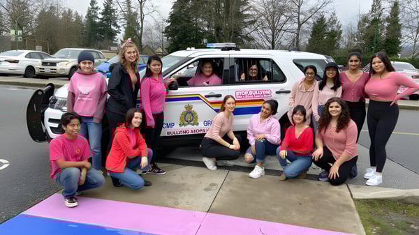 Un grupo de alumnas de la Cariboo Hill School posan frente a un vehículo policial al aire libre.