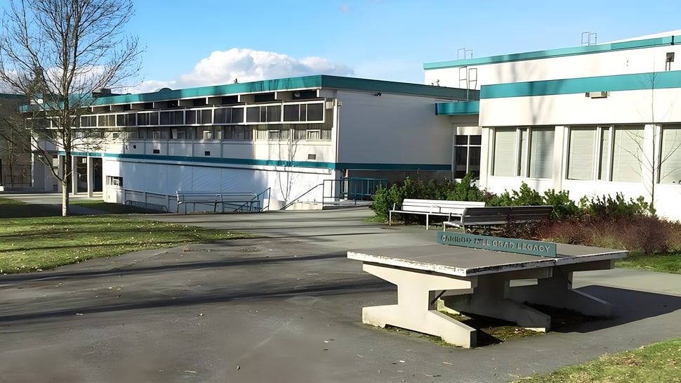 El moderno edificio de varios pisos de la Cariboo Hill School está rodeado de un área pavimentada con un banco de concreto.