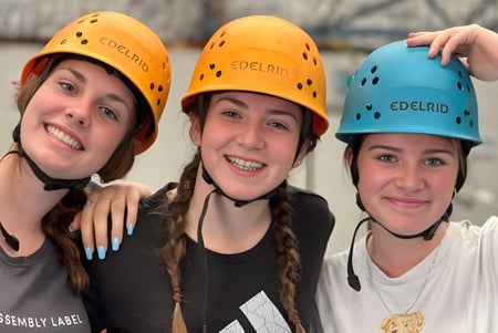 Tres alumnas de la Carine Senior High School llevan cascos amarillos y azules y posan juntas en un interior.