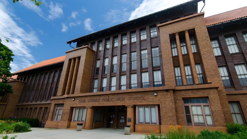 El edificio de ladrillo de varios pisos de la Carl Schurz High School se encuentra en un área exterior bien cuidada con plantas verdes.