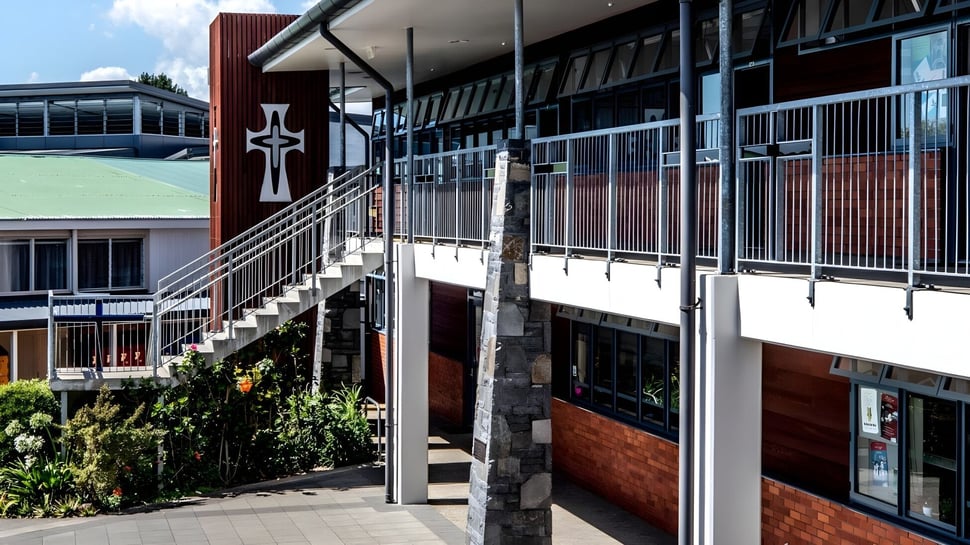 El moderno edificio de varios pisos con diseño en forma de cruz en el campus del Carmel College está rodeado de áreas verdes y un camino pavimentado.