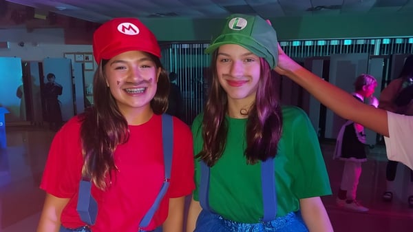 Dos estudiantes de la Carrefour de l’Acadie llevan disfraces coloridos y posan en una fiesta de carnaval en el edificio escolar.