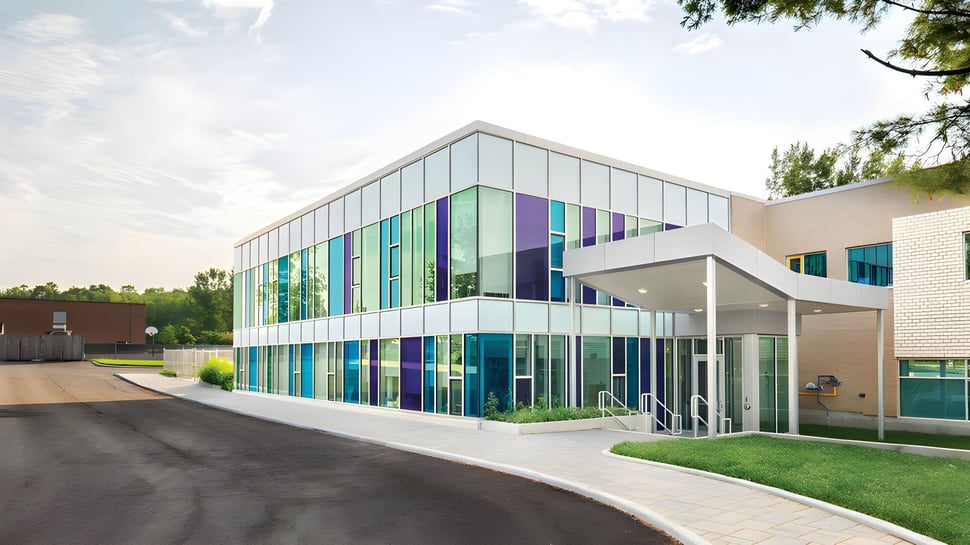 El edificio escolar de varios pisos de la École secondaire publique Carrefour Jeunesse con fachada de vidrio y paneles de colores se encuentra en un entorno verde.