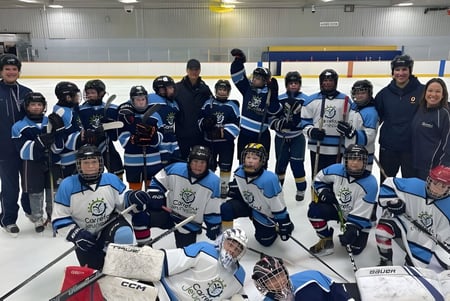 Un grupo de jóvenes jugadores y jugadoras de hockey posan en la pista de hielo de la École secondaire publique Carrefour Jeunesse.
