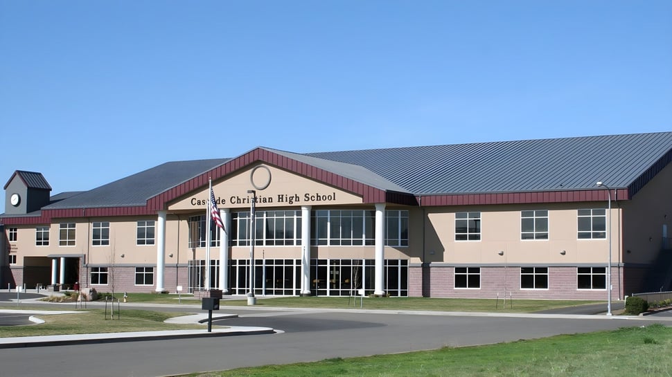 El moderno edificio escolar de la Cascade Christian High School con techo de tejas rojas y fachada de vidrio bajo un cielo despejado.