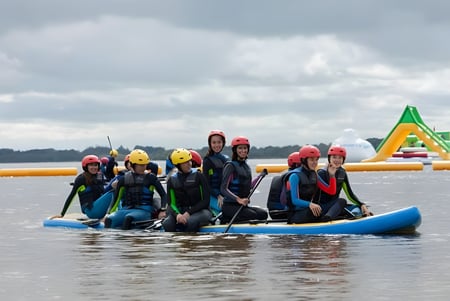 Estudiantes de la Castlerea Community School reman juntos en coloridos chalecos salvavidas en una balsa durante una actividad al aire libre.