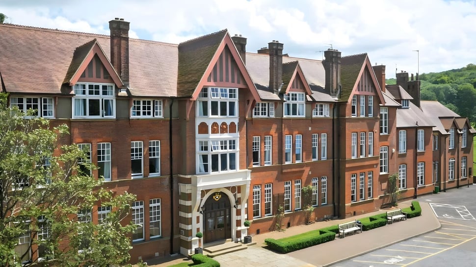El edificio de ladrillo de varios pisos de la Caterham School muestra arquitectura Tudor y está rodeado de áreas verdes.