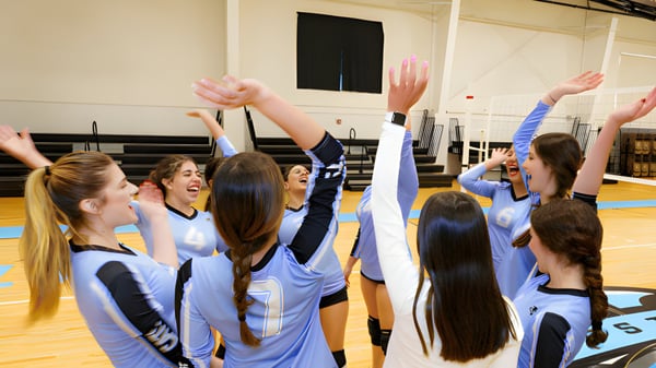 Un grupo de jóvenes atletas en uniformes azules entrena juntas en el gimnasio de la CATS Academy Boston.