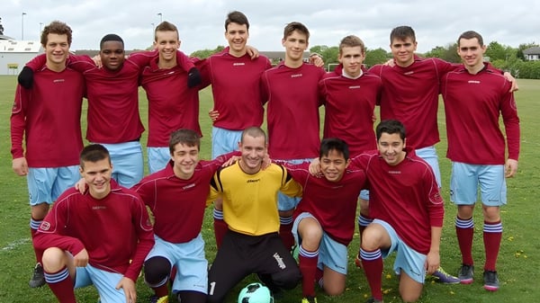 Un grupo de estudiantes de CATS Cambridge está juntos en un campo de fútbol con camisetas rojas.