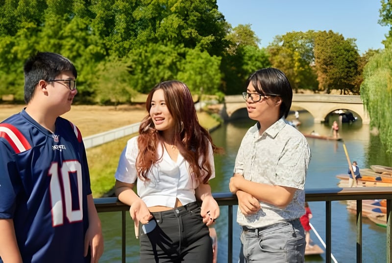 Tres estudiantes de CATS Cambridge están juntos y conversan en un área similar a un parque con árboles y agua.