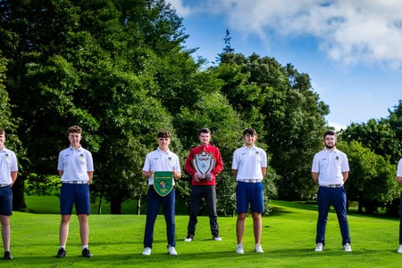 Estudiantes de la C.B.S. Roscommon están en uniformes deportivos en un campo verde bajo un cielo azul.