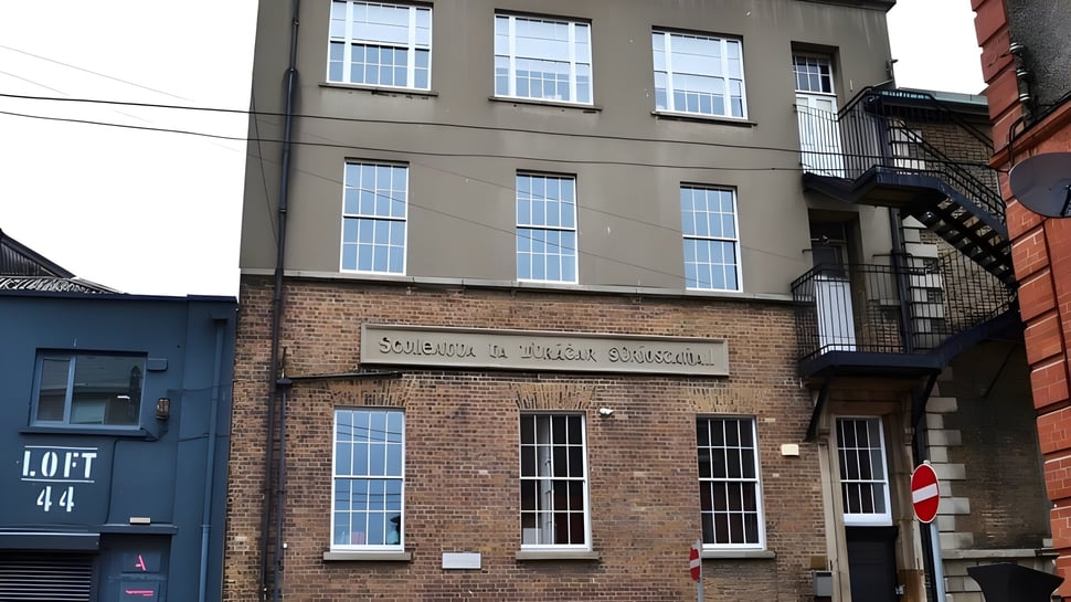 El edificio de ladrillo de varios pisos con grandes ventanas en el terreno de CBS Westland Row en un entorno urbano.
