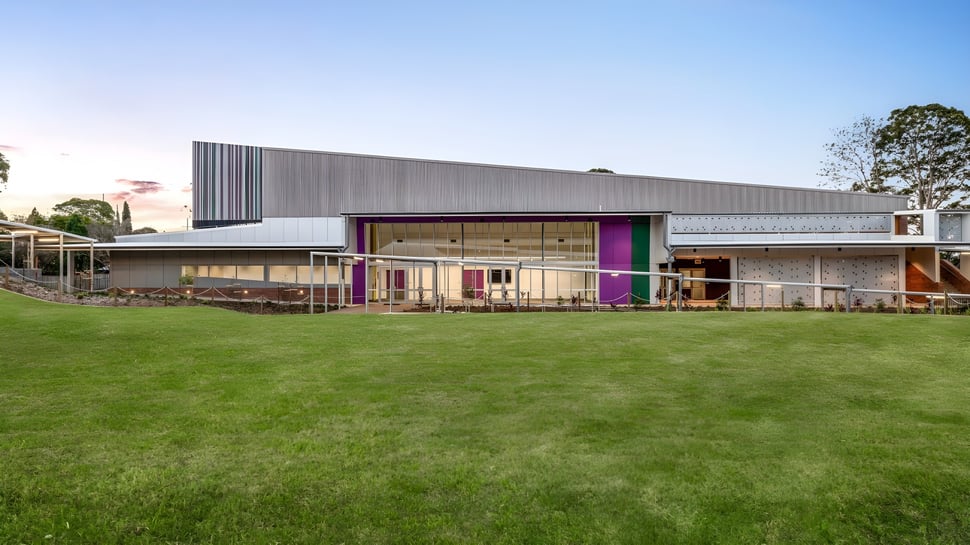 El moderno edificio de una planta de la Centenary Heights State High School, con una gran superficie de césped en el frente, está rodeado de árboles.