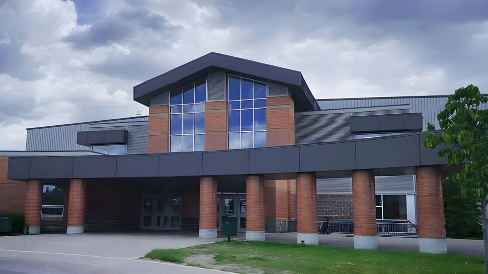 El moderno edificio de varios pisos del Centennial Collegiate con una fachada de ladrillo y vidrio está rodeado de áreas de césped y árboles.