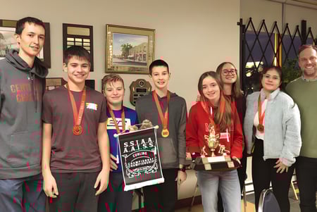 Un grupo de estudiantes de la Centennial Regional High School sostiene en el edificio escolar varios premios y trofeos.