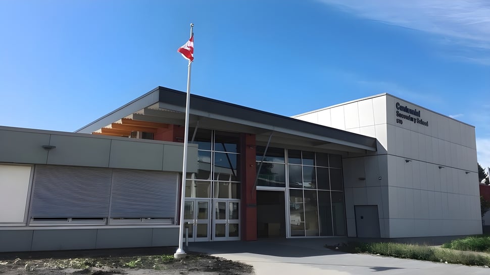 El moderno edificio de la Centennial Secondary School en British Columbia con una bandera canadiense frente a un cielo azul claro.