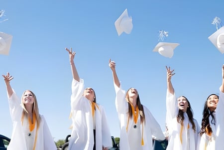 Estudiantes de la Centerville Senior High School celebran con los brazos en alto bajo un cielo azul con globos blancos.