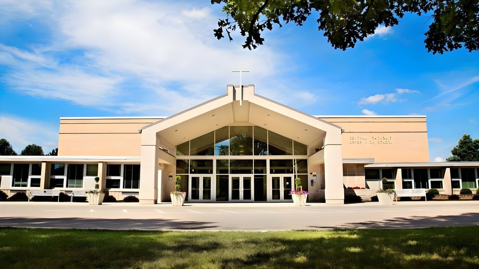 El moderno edificio principal de la Central Catholic Jr.-Sr. High School con grandes ventanas y área verde circundante bajo un cielo azul.