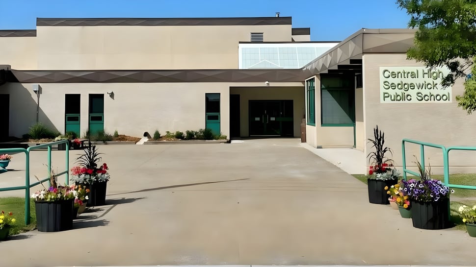 El moderno edificio escolar de la Central High Sedgewick Public School con entrada pavimentada y flores está rodeado de árboles.
