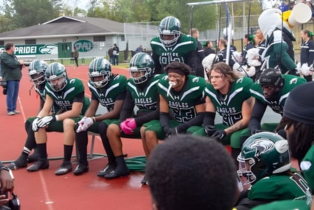 Un grupo de jóvenes atletas de la Central Methodist University se reúne en uniformes verdes en el campo de deportes.