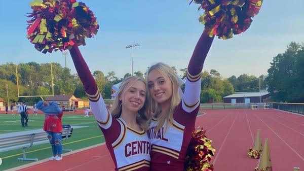 Dos animadoras de la Central Regional High School están de pie con pompones en el campo deportivo frente al estadio.