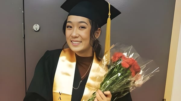 Una graduada de Central Technical School en toga sostiene un ramo de rosas rojas frente a una puerta y sonríe.
