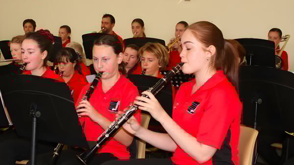 Estudiantes de la Central Yorke School en uniformes rojos tocan como un ensamble musical en un escenario.