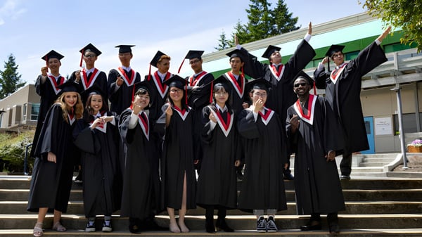 Los graduados de la Centre Dufferin District High School están de pie en togas negras con estolas rojas en las escaleras del edificio escolar.
