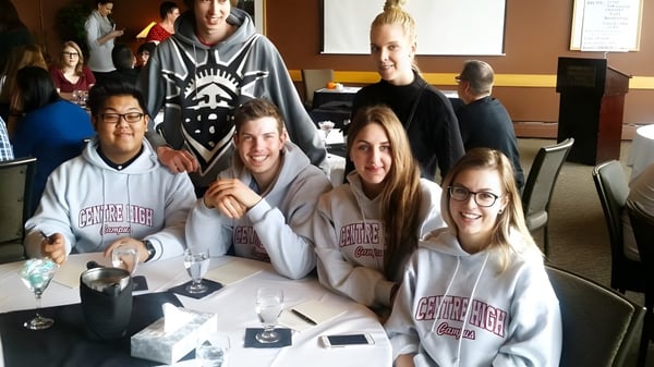 Un grupo de estudiantes se sienta en la mesa del aula del Centre High Campus con bebidas y dispositivos electrónicos.