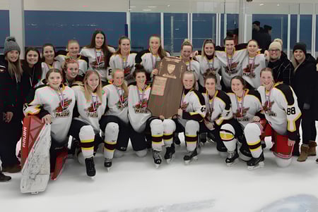 Un grupo de jóvenes jugadoras de hockey de la Centre Wellington District High School está en el hielo celebrando con un trofeo.