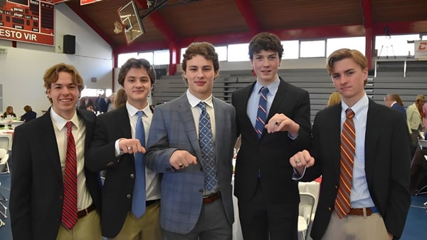 Un grupo de estudiantes de la Chaminade College Preparatory School está junto en un pasillo escolar con una canasta de baloncesto al fondo.