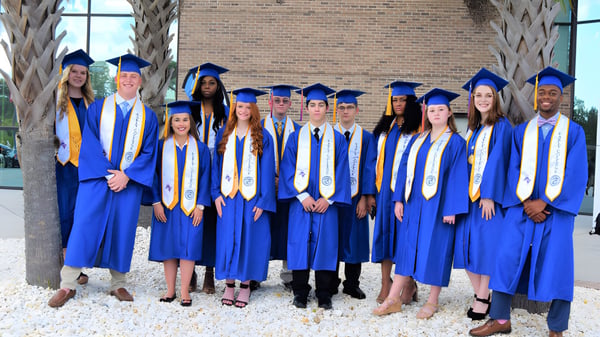 Los graduados del Chancellor State College celebran su graduación frente a un edificio de ladrillos.