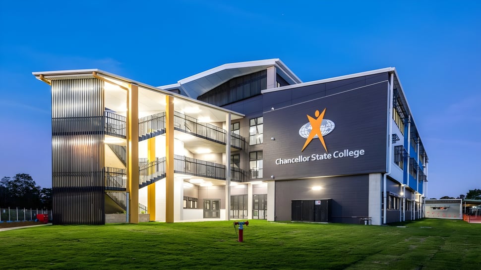 El moderno edificio de varios pisos del Chancellor State College bajo un cielo azul claro en un área de césped iluminada.
