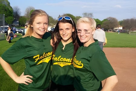 Tres alumnas de The Charles Finney School están juntas en el campo deportivo con un campo de béisbol al fondo.