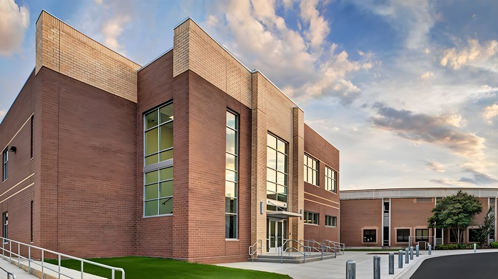 El moderno edificio de ladrillo de las Charlotte-Mecklenburg Schools con grandes ventanas y una superficie de césped en primer plano bajo un cielo nublado.