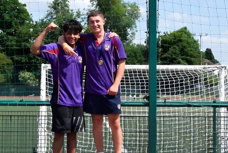 Dos estudiantes de la Chase Grammar School están frente a una portería de fútbol en un campo de césped con árboles al fondo.