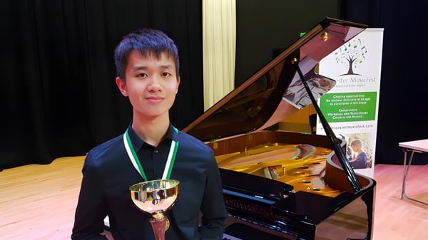 Un estudiante de la Chase Grammar School está frente a un piano de cola y sostiene un trofeo en la mano.