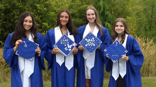 Cuatro estudiantes en togas de graduación azules están juntas en el área verde de la Chatelech Secondary School.