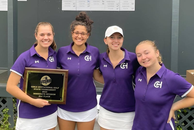 Cuatro alumnas de la Chatham Hall School sostienen con orgullo un trofeo frente a un edificio escolar con carteles.