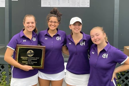 Cuatro alumnas de la Chatham Hall School en uniformes violetas sostienen un trofeo frente a un edificio.